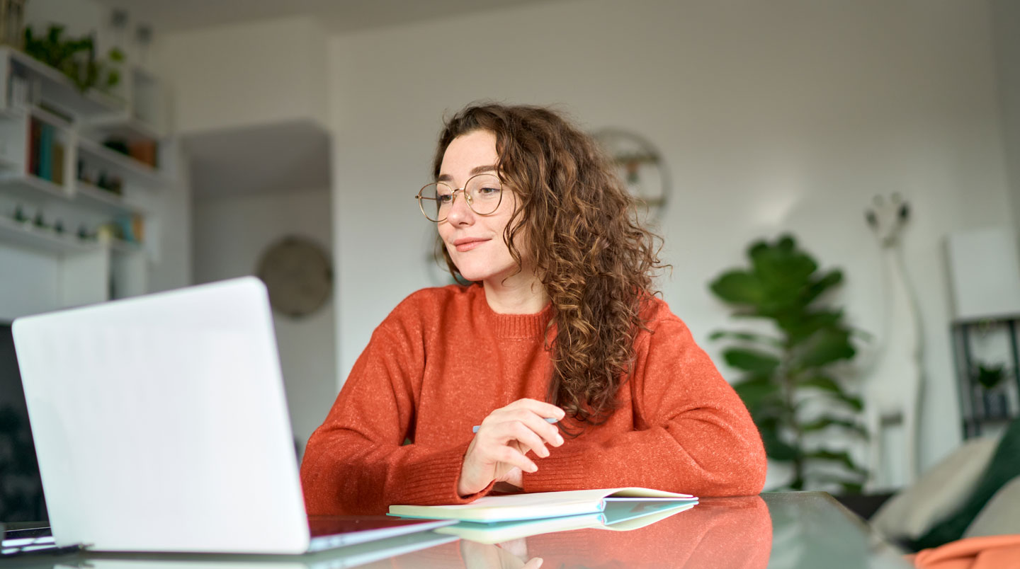 Bureau à domicile organisé avec ordinateur portable affichant une interface de formation en ligne en décoration, carnet de notes, et matériel d'apprentissage dans un environnement lumineux